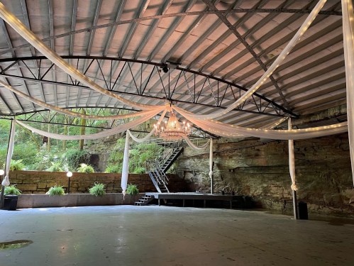 An indoor venue with draped fabric, a chandelier, and a staircase against a natural rock backdrop.