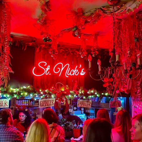 Cozy bar scene with festive decorations and a glowing "St. Nick's" sign, illuminated in red light.