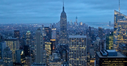 A panoramic view of New York City at dusk, featuring the Empire State Building and illuminated skyscrapers.