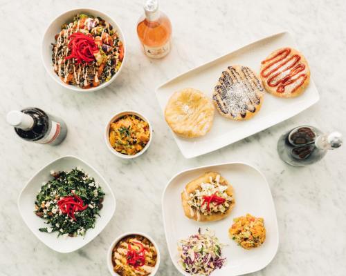 A variety of colorful dishes including salads, tacos, and pastries arranged on a marble table with drinks.
