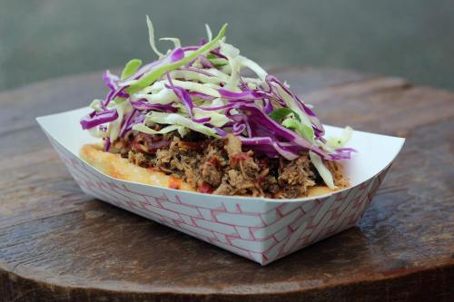 A delicious taco topped with shredded cabbage and seasoned meat, served in a paper tray on a wooden surface.