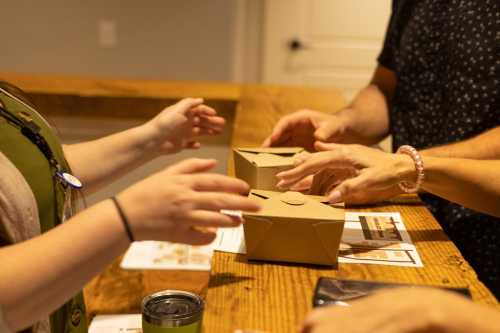 Two people exchanging takeout boxes at a wooden counter, with hands reaching out to each other.