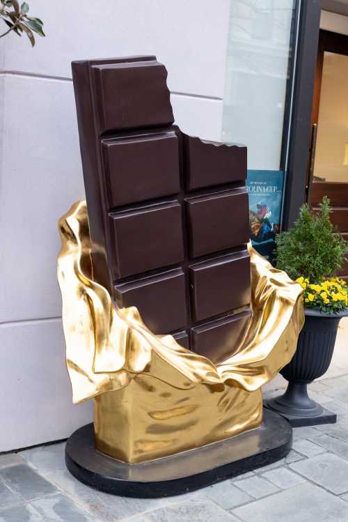 A large chocolate bar sculpture partially wrapped in golden fabric, displayed outside a store.