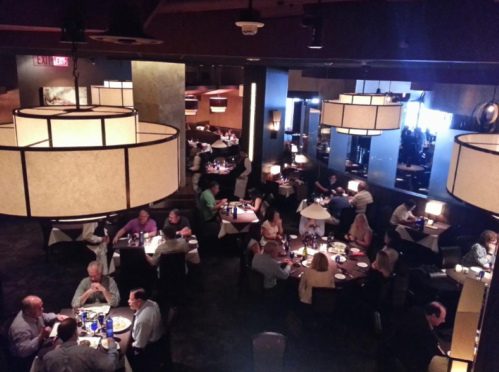 A dimly lit restaurant with large chandeliers, featuring diners at tables enjoying meals and conversation.