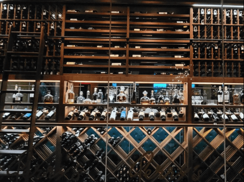 A wooden wine rack displaying various bottles of wine and spirits in an elegant setting.