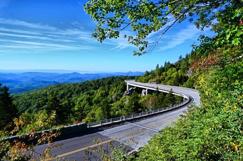 A winding road curves through lush green mountains under a clear blue sky.