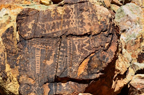 Petroglyphs carved into a rocky surface, featuring geometric patterns and figures in earthy tones.