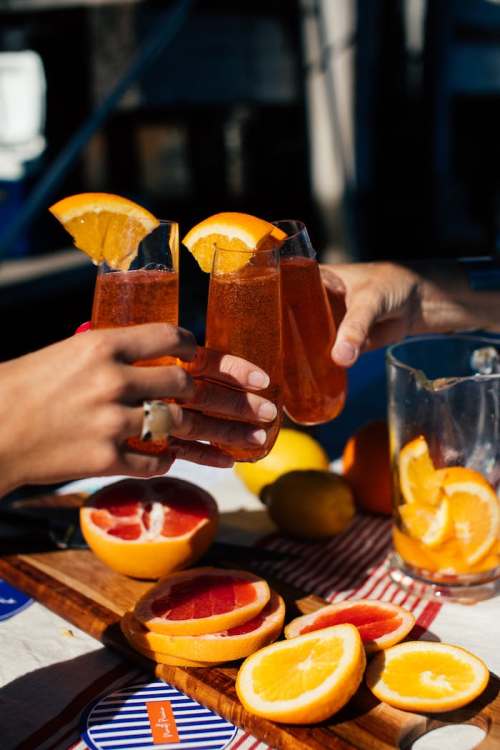 Three glasses of orange drinks are clinked together, surrounded by fresh citrus fruits on a table.