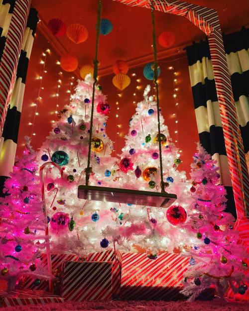 A festive scene with two white Christmas trees adorned with colorful ornaments, a swing, and vibrant decorations.