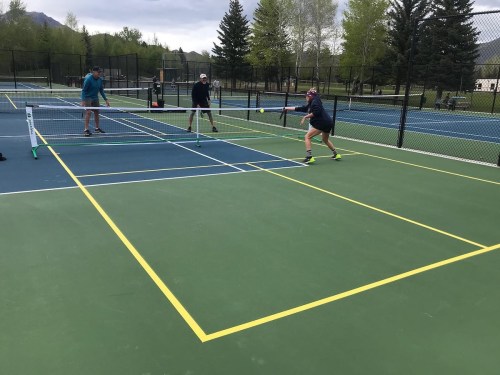 A group of people playing tennis on an outdoor court, with one player hitting the ball while others watch.