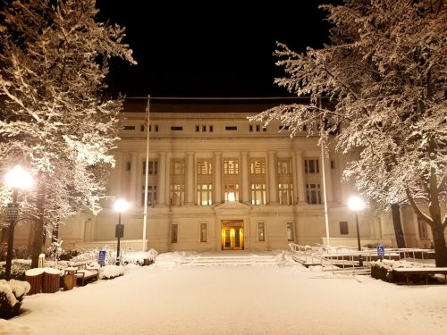 A snow-covered building at night, illuminated by streetlights, with trees lining the path and a peaceful atmosphere.