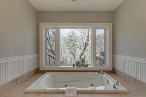 A spacious bathroom featuring a large bathtub with a scenic view through a large window.