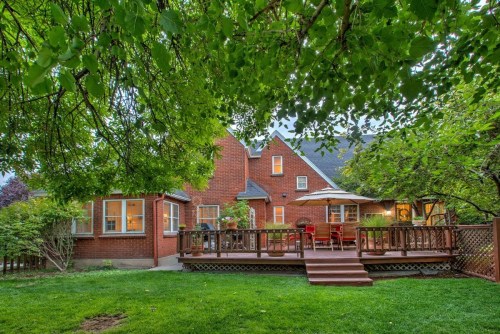 A cozy brick house with a wooden deck, surrounded by lush greenery and trees in a serene backyard setting.