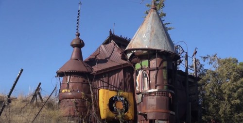 A whimsical, rusted metal structure resembling a fairytale castle, set against a clear blue sky.