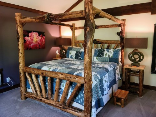 A rustic bedroom featuring a wooden four-poster bed, patterned bedding, and modern lamps on side tables.