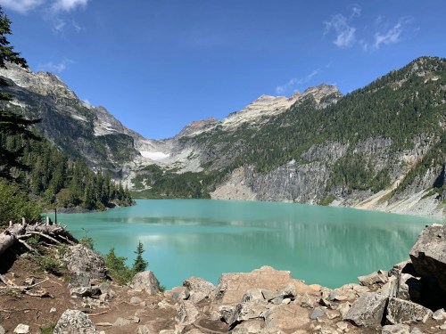 A serene turquoise lake surrounded by mountains and lush greenery under a clear blue sky.