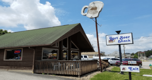 A wooden building with a green roof, featuring signs for "Root Beer Shack" and an open sign, under a blue sky.