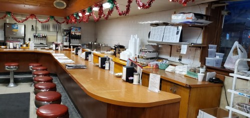 A cozy diner interior with a wooden counter, red stools, and festive decorations along the walls.