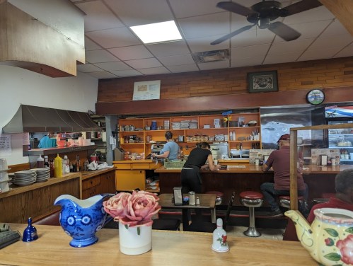 A cozy diner interior with a counter, patrons seated, and staff preparing food in a warm, inviting atmosphere.