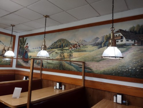 Interior of a restaurant featuring wooden booths, pendant lights, and a scenic mural of mountains and countryside.