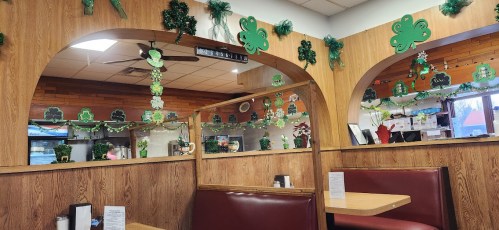 Interior of a restaurant decorated with green shamrocks and festive greenery, featuring wooden arches and red booths.
