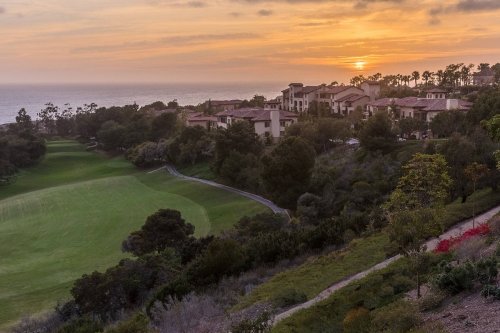 A scenic view of a golf course at sunset, with lush greenery and coastal homes in the background.