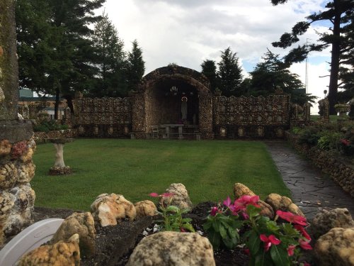 A serene garden with a stone structure, surrounded by trees and colorful flowers in the foreground.