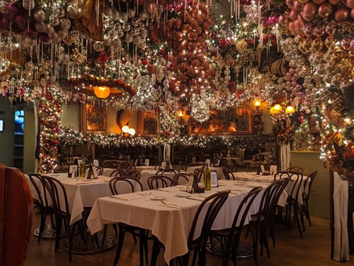 A festive restaurant interior adorned with colorful decorations and twinkling lights, featuring tables set for dining.