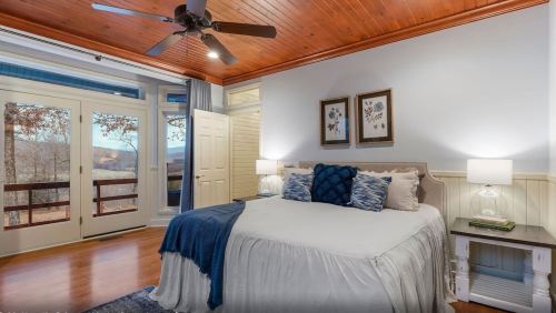 Cozy bedroom with a queen bed, wooden ceiling, and large windows showcasing a scenic view.