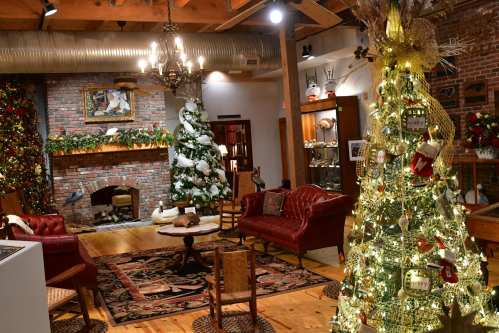 Cozy holiday-themed room with a decorated Christmas tree, festive decor, and a fireplace surrounded by greenery.