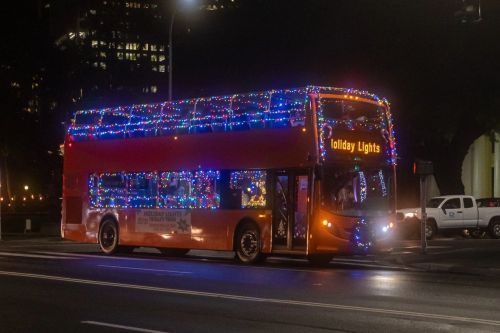 A brightly lit double-decker bus decorated with holiday lights driving through a city at night.