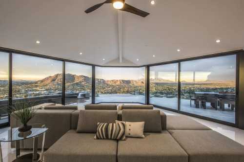 Modern living room with a sectional sofa, large windows showcasing a mountain view, and a sleek design.