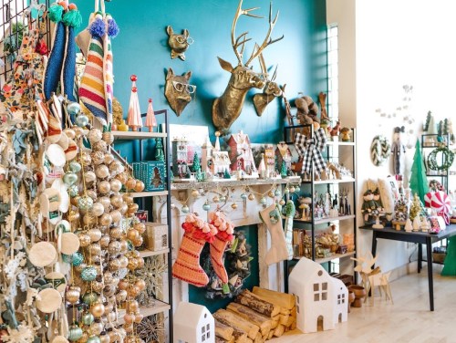 A festive shop display with colorful decorations, a decorated tree, and holiday-themed items on shelves and a mantel.