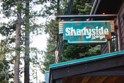 Sign for "Shadyside Lounge" hanging from a building, surrounded by tall trees in a forested area.