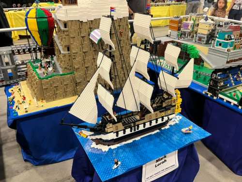 A detailed LEGO ship on a blue base, surrounded by colorful LEGO scenes, including a mountain and a hot air balloon.