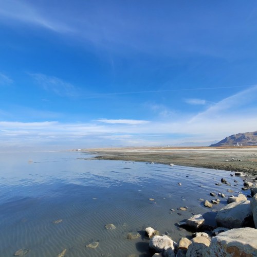 A serene landscape featuring calm water, rocky shorelines, and a clear blue sky with distant mountains.