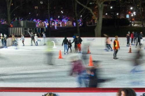 A busy ice skating rink with skaters in motion, surrounded by festive lights and orange cones.