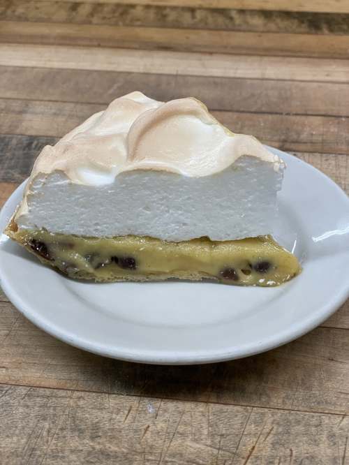 A slice of pie with a golden custard filling and a fluffy meringue topping on a white plate.