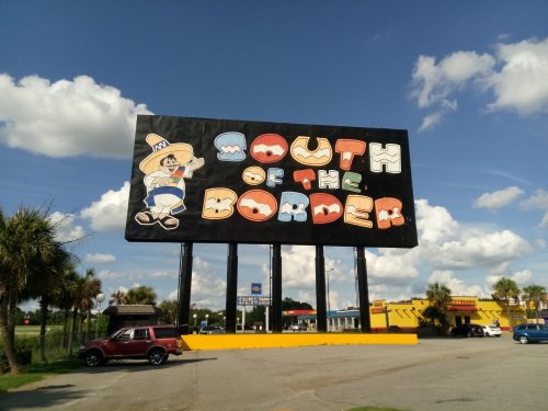 A large colorful billboard reading "South of the Border" with a cartoon character, set against a blue sky and palm trees.