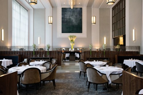Elegant restaurant interior with round tables, plush chairs, and a large floral arrangement in a modern, airy space.