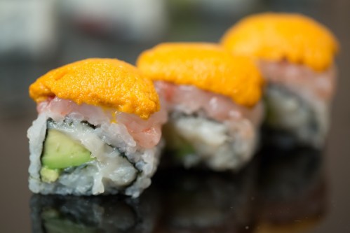 Three sushi rolls topped with bright orange uni, showcasing layers of fish and avocado.