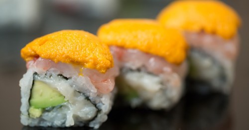 Three sushi rolls topped with bright orange uni, showcasing layers of fish and avocado wrapped in seaweed.