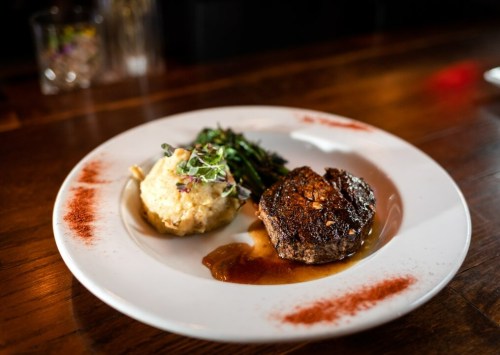 A plate featuring a seared steak, creamy mashed potatoes, and sautéed greens, garnished with microgreens.