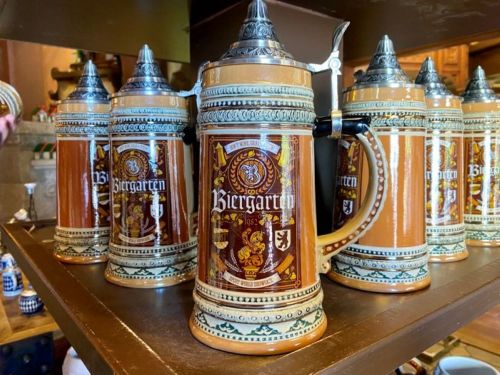 A collection of decorative beer steins with "Biergarten" design, displayed on a wooden shelf.
