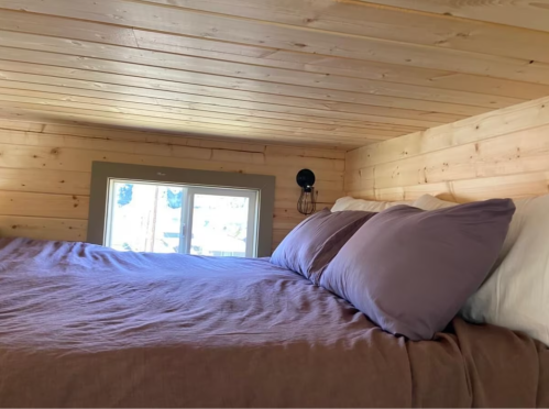 Cozy loft bedroom with a wooden ceiling, large bed, and a window letting in natural light.