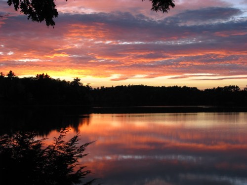 A serene lake at sunset, reflecting vibrant orange and purple clouds against a tranquil landscape.