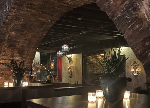 Cozy restaurant interior with stone arches, dim lighting, plants, and decorative lanterns.