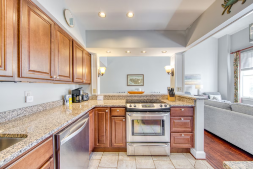 Modern kitchen with granite countertops, stainless steel appliances, and wooden cabinets, leading to a cozy living area.