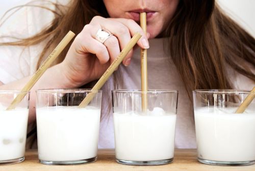 A person sipping from a glass with a bamboo straw, surrounded by three similar glasses filled with a white beverage.