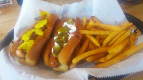 Two hot dogs topped with pickles and jalapeños, served with a side of golden French fries in a basket.